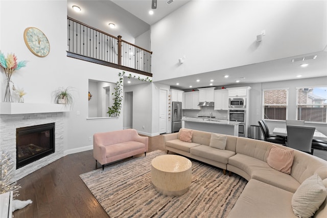 living area featuring dark wood-style flooring, visible vents, a towering ceiling, a stone fireplace, and baseboards