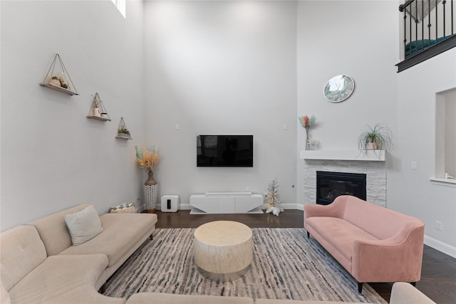 living area with baseboards, a towering ceiling, a tiled fireplace, and wood finished floors