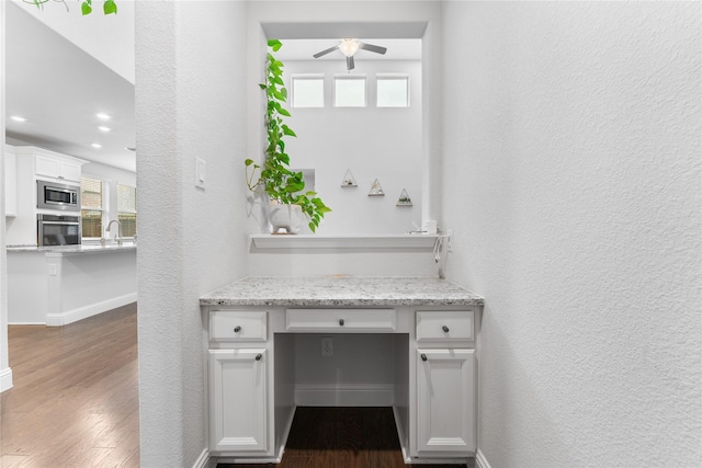 unfurnished office featuring baseboards, a textured wall, dark wood-style floors, ceiling fan, and a sink