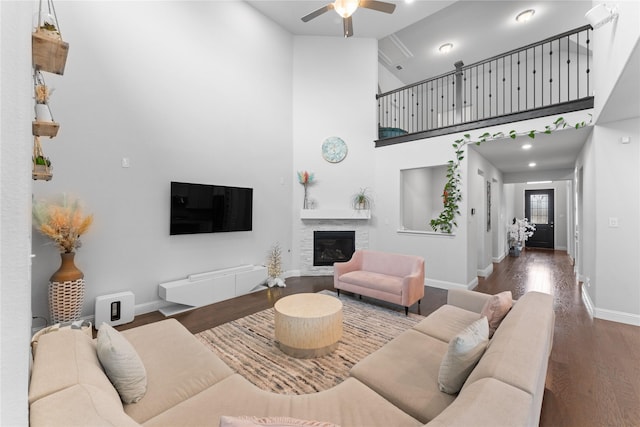 living area featuring a high ceiling, a ceiling fan, baseboards, dark wood-style floors, and a glass covered fireplace