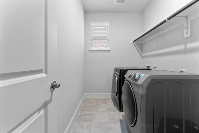 washroom with light tile patterned floors, laundry area, washing machine and dryer, and baseboards