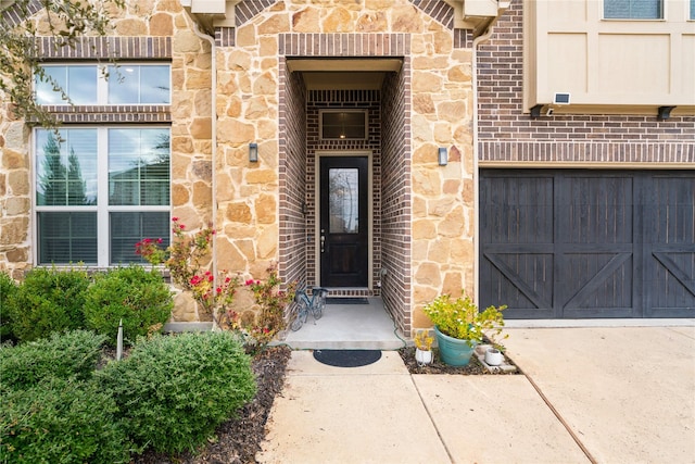 property entrance with a garage, stone siding, concrete driveway, and brick siding