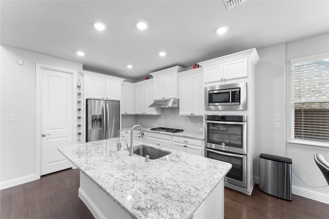 kitchen featuring an island with sink, stainless steel appliances, under cabinet range hood, white cabinetry, and a sink