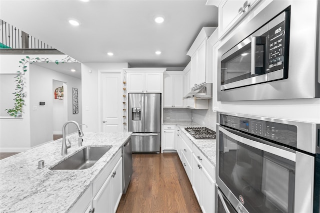 kitchen with light stone counters, appliances with stainless steel finishes, white cabinets, a sink, and under cabinet range hood