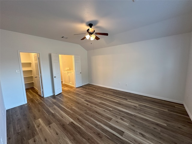 unfurnished bedroom featuring ceiling fan, vaulted ceiling, dark hardwood / wood-style floors, a walk in closet, and a closet