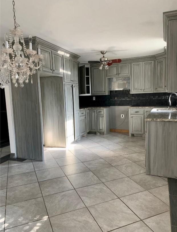 kitchen with gray cabinets, light tile patterned flooring, ceiling fan with notable chandelier, tasteful backsplash, and sink