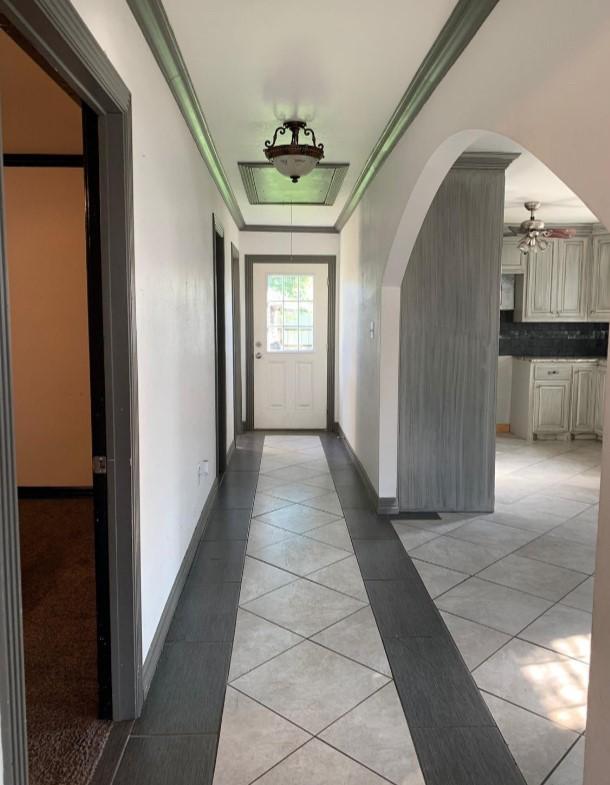 hall featuring ornamental molding, light tile patterned flooring, and a tray ceiling