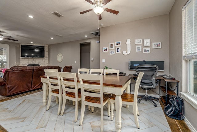 dining room featuring ceiling fan, a fireplace, and light parquet floors