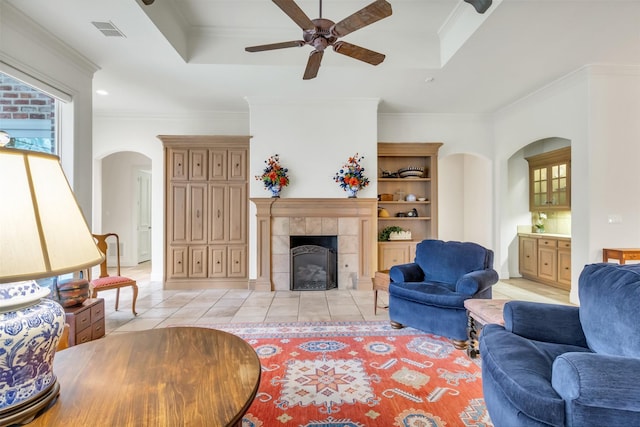 living room with crown molding, a fireplace, a tray ceiling, and light tile patterned flooring