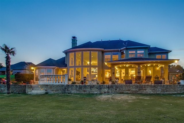 back house at dusk featuring a patio and a lawn