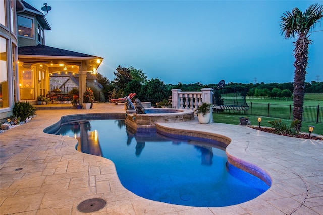 pool at dusk featuring an in ground hot tub and a patio