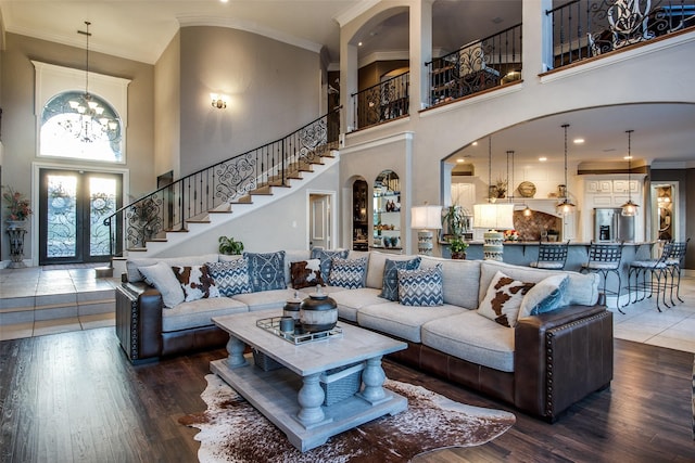 living room featuring french doors, crown molding, an inviting chandelier, hardwood / wood-style flooring, and a high ceiling