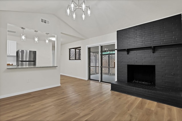 unfurnished living room featuring hardwood / wood-style flooring, lofted ceiling, a brick fireplace, and a notable chandelier