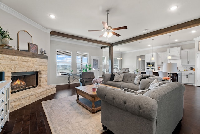 living room featuring crown molding, dark wood-type flooring, ceiling fan, a stone fireplace, and beamed ceiling