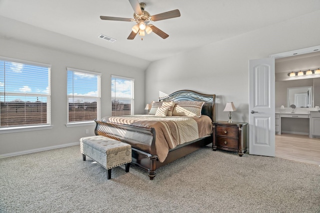 bedroom featuring ceiling fan, light colored carpet, ensuite bathroom, and vaulted ceiling