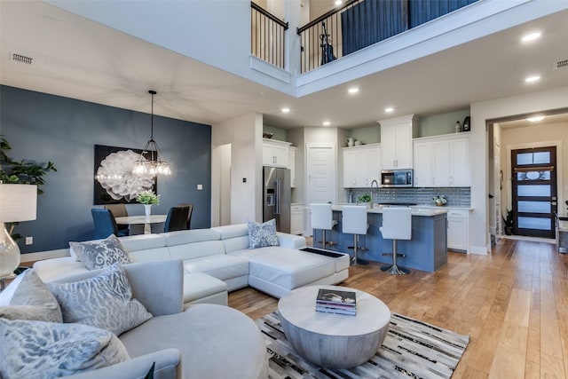 living room featuring a towering ceiling, an inviting chandelier, and light hardwood / wood-style flooring