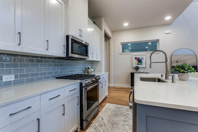 kitchen featuring white cabinetry, sink, backsplash, light hardwood / wood-style floors, and stainless steel appliances