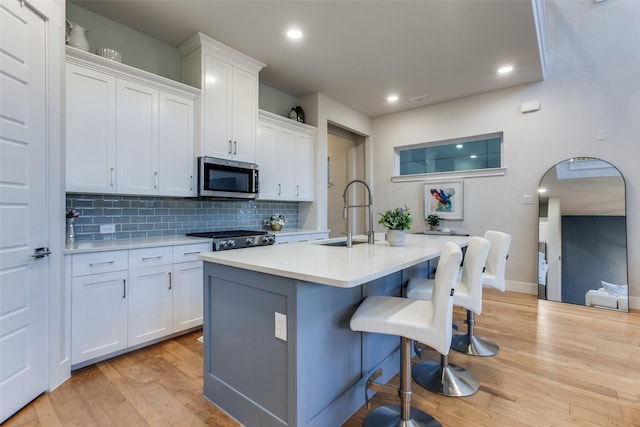 kitchen featuring a breakfast bar, sink, a center island with sink, light hardwood / wood-style floors, and white cabinets