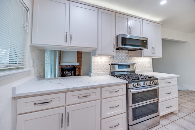 kitchen with white cabinetry, light stone counters, tasteful backsplash, light tile patterned floors, and stainless steel appliances