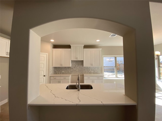 kitchen featuring sink, backsplash, white cabinets, and light stone counters