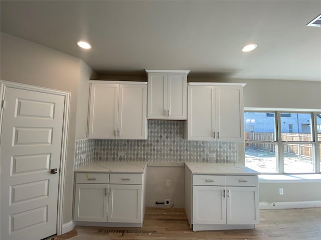 kitchen featuring tasteful backsplash, light stone countertops, white cabinets, and light wood-type flooring