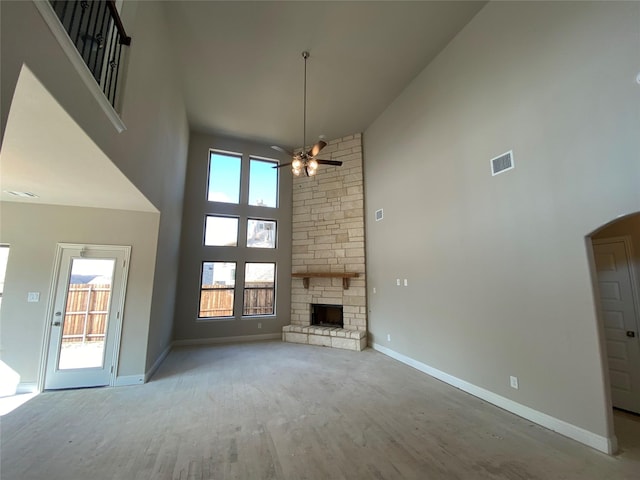 unfurnished living room with a stone fireplace, light hardwood / wood-style flooring, ceiling fan, and a towering ceiling