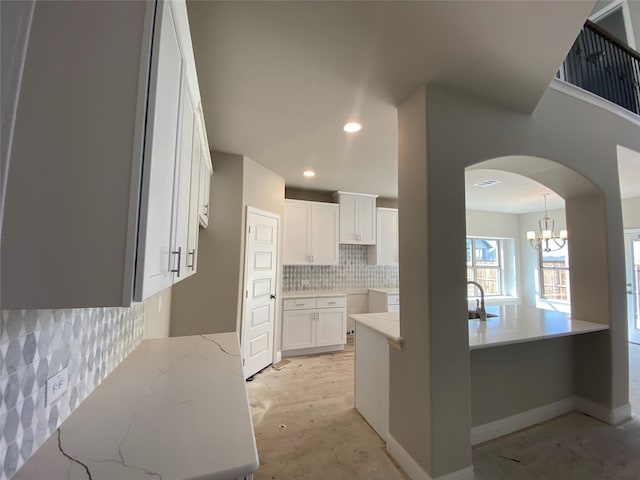 kitchen with sink, a notable chandelier, light stone countertops, decorative backsplash, and white cabinets