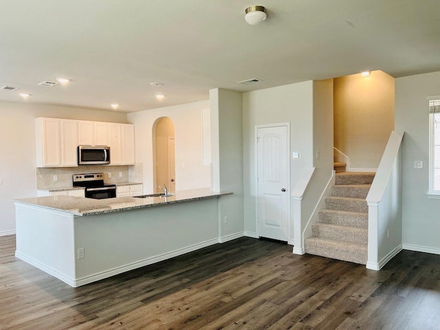 kitchen with dark wood-type flooring, light stone counters, appliances with stainless steel finishes, kitchen peninsula, and white cabinets