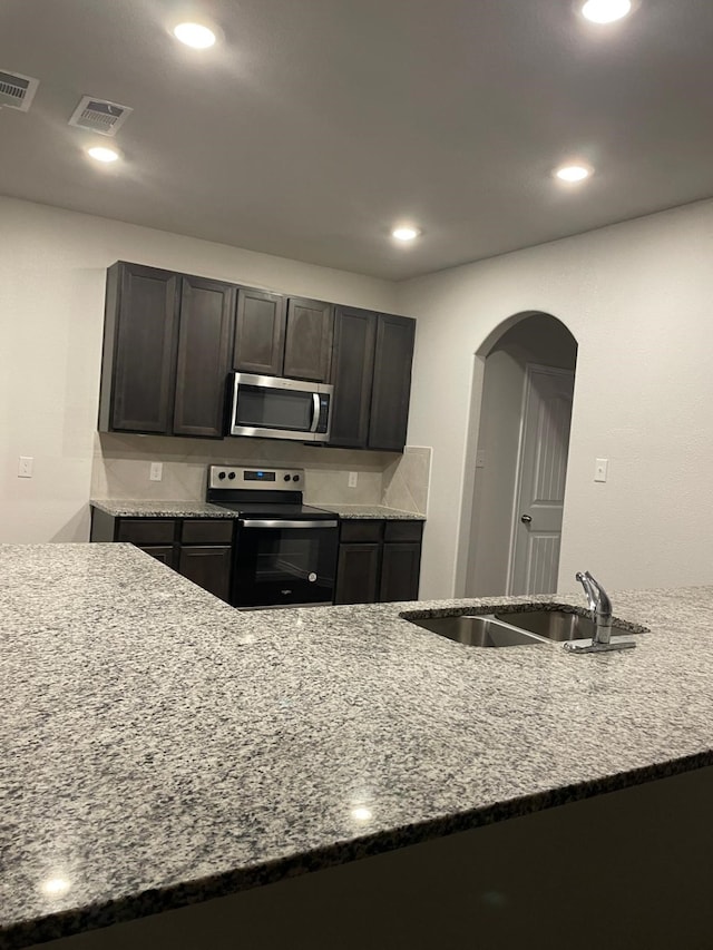 kitchen with light stone counters, electric range oven, dark brown cabinets, and sink