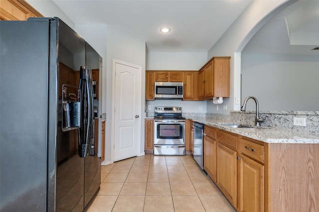 kitchen with light tile patterned floors, stainless steel appliances, light stone counters, and sink