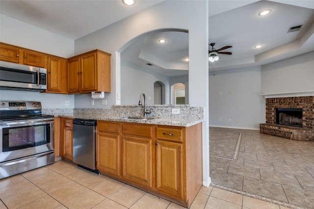 kitchen featuring appliances with stainless steel finishes, sink, ceiling fan, a raised ceiling, and light stone countertops