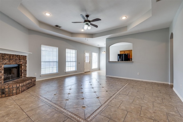 unfurnished living room featuring a tray ceiling, ceiling fan, a fireplace, and light tile patterned floors