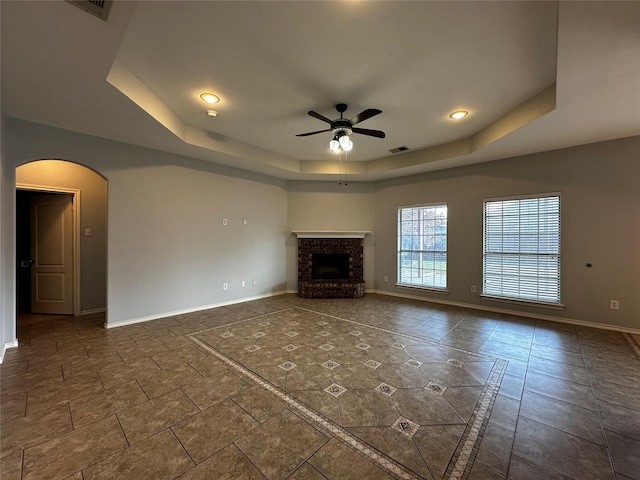 unfurnished living room with a raised ceiling, a brick fireplace, and ceiling fan