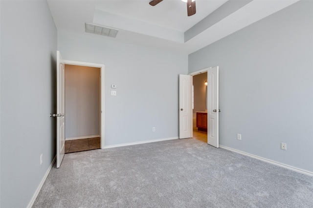 unfurnished bedroom with light carpet, connected bathroom, ceiling fan, and a raised ceiling