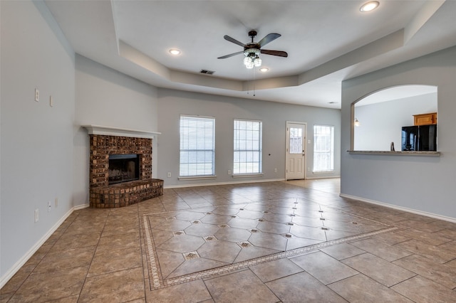 unfurnished living room featuring a tray ceiling, a fireplace, ceiling fan, and light tile patterned floors