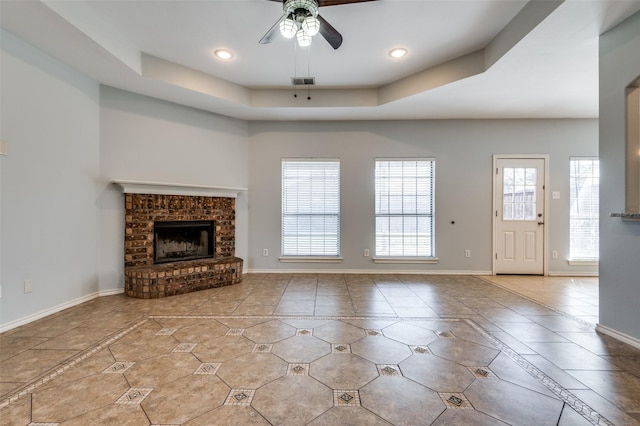 unfurnished living room featuring ceiling fan, light tile patterned flooring, a raised ceiling, and a wealth of natural light