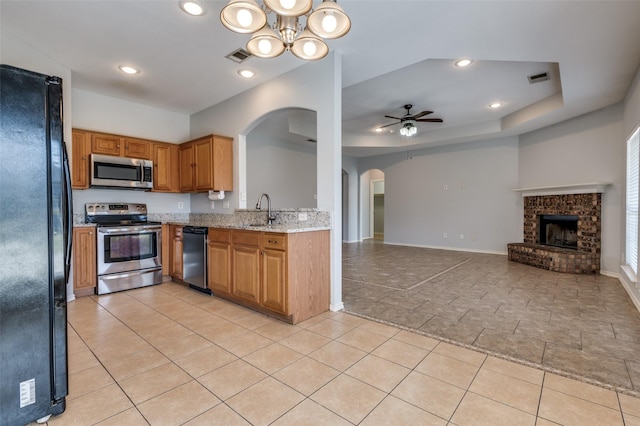 kitchen featuring a brick fireplace, appliances with stainless steel finishes, sink, light stone counters, and ceiling fan