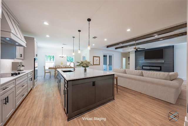 kitchen featuring pendant lighting, sink, custom exhaust hood, a kitchen island with sink, and black appliances