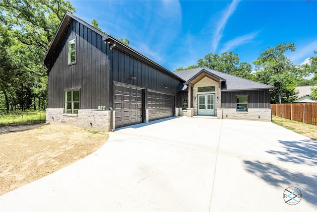 modern farmhouse featuring fence, driveway, french doors, stone siding, and a garage