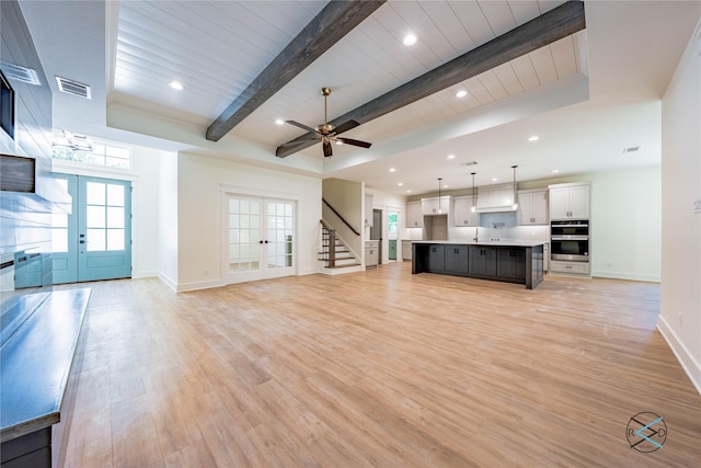 unfurnished living room with beamed ceiling, french doors, stairs, and light wood-style floors