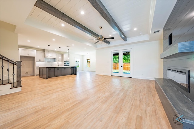 unfurnished living room featuring visible vents, baseboards, light wood-type flooring, stairs, and beam ceiling