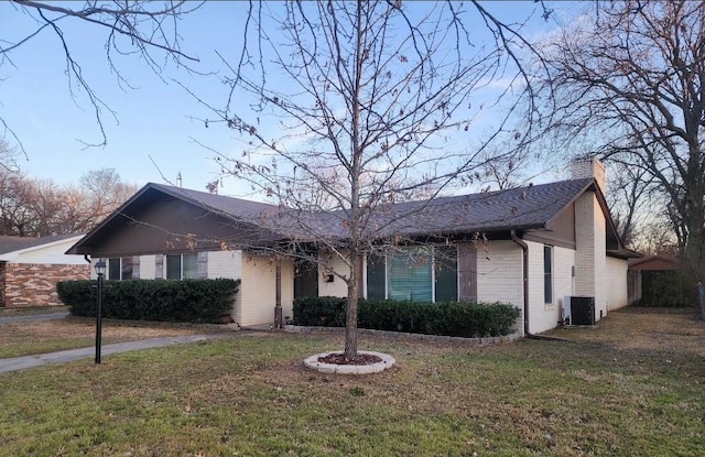 ranch-style house with a front yard, a chimney, central AC, and brick siding