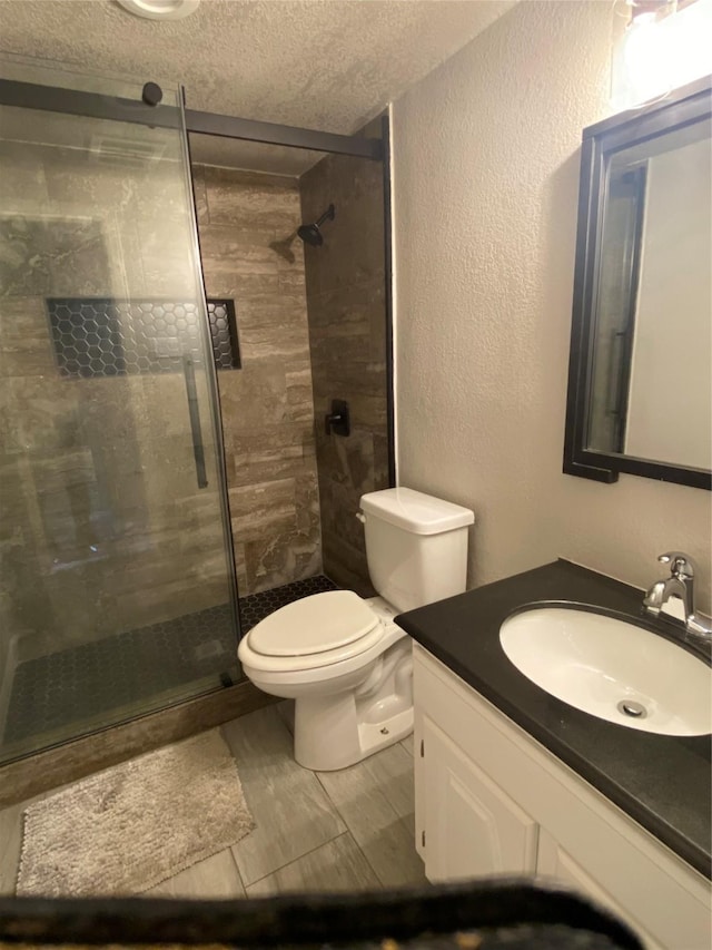 bathroom with vanity, toilet, a textured ceiling, and tiled shower