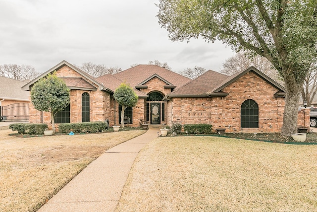 view of front of house with a shingled roof, a front yard, and brick siding