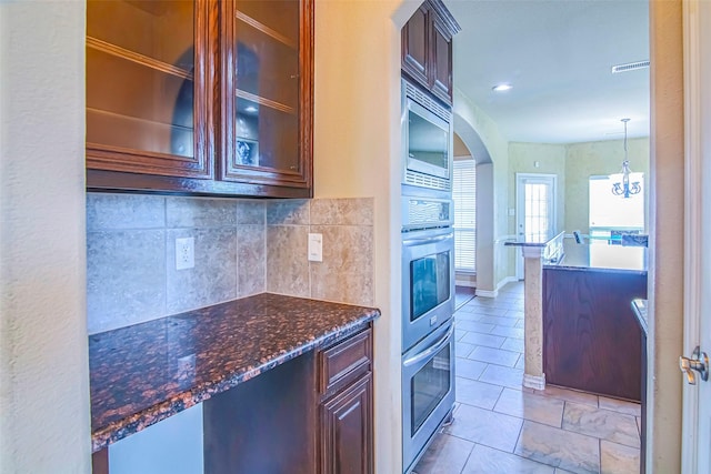 kitchen with pendant lighting, stainless steel microwave, dark stone countertops, backsplash, and light tile patterned floors