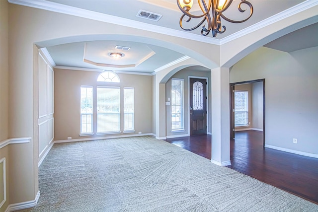 entrance foyer with an inviting chandelier, ornamental molding, a tray ceiling, and dark colored carpet