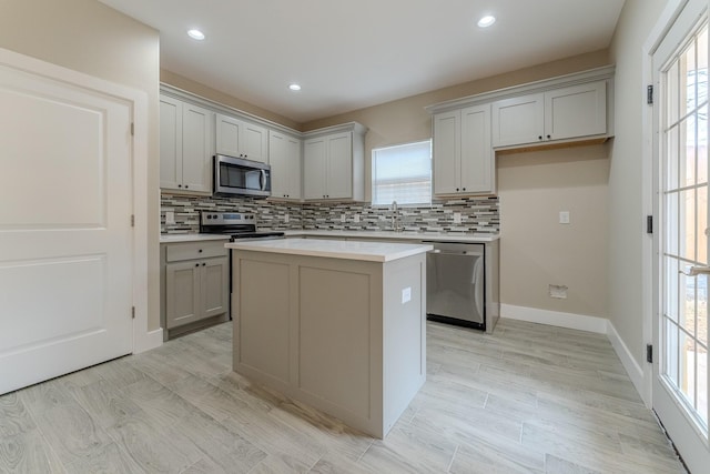 kitchen with light hardwood / wood-style flooring, appliances with stainless steel finishes, gray cabinets, a kitchen island, and backsplash