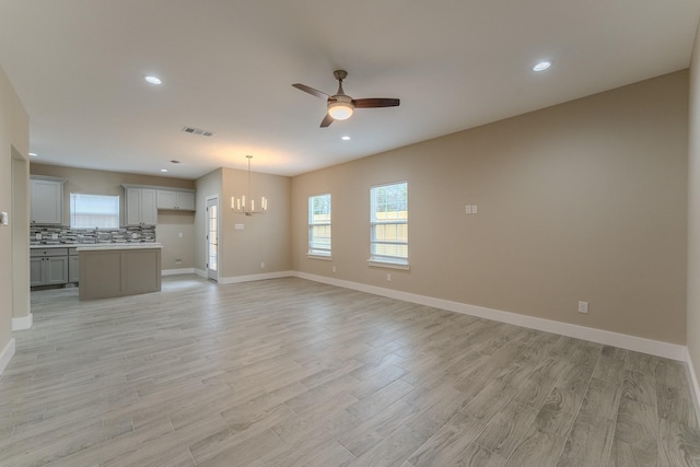 unfurnished living room featuring sink, ceiling fan with notable chandelier, and light wood-type flooring