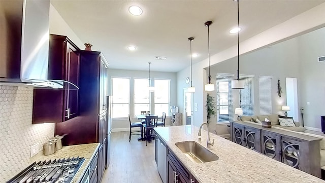 kitchen featuring appliances with stainless steel finishes, pendant lighting, sink, exhaust hood, and light stone countertops