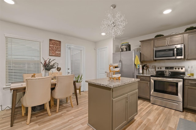 kitchen with appliances with stainless steel finishes, decorative light fixtures, a center island, a notable chandelier, and light hardwood / wood-style floors